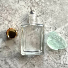 Load image into Gallery viewer, This bulk perfume bottle has a thin roller ball display. A steel roller ball insert and a gold cap next to it.