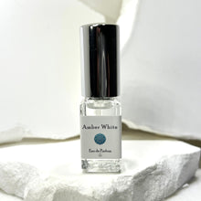 Load image into Gallery viewer, Amber White eau de parfum bottle on a white stone surface with a blurred white background.