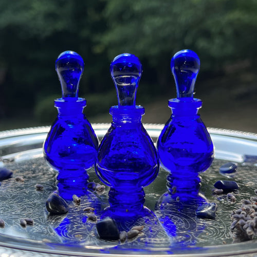 Cobalt Blue Glass Potion Genie Bottles on a silver tray sparkling in the sunshing. Imagine colorful perfume oils inside.