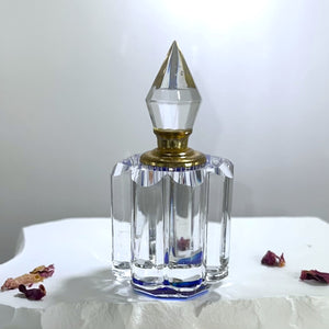 An empty perfume bottle that is a refillable perfume bottle for attar perfume. Clear, blue base, pointed top.