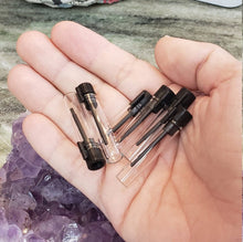 Load image into Gallery viewer, Several Glass vials in a human hand to see a general size comparison. Clear glass scientific vials with black applicator wands.
